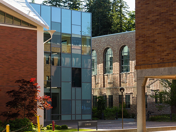 Intersection of campus buildings, traditional brick mixed with glass exterior, red leafed tree in foreground