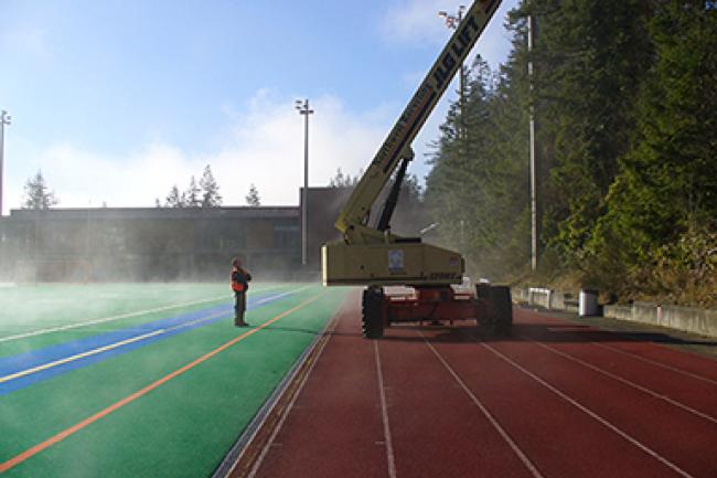 Maintenance worker watching lift equipment in use on an athletic track on a misty morning