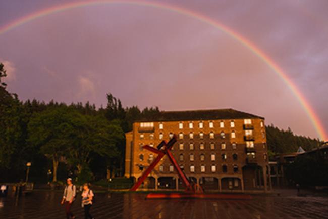 Rainbow over red sculpture and brick campus building